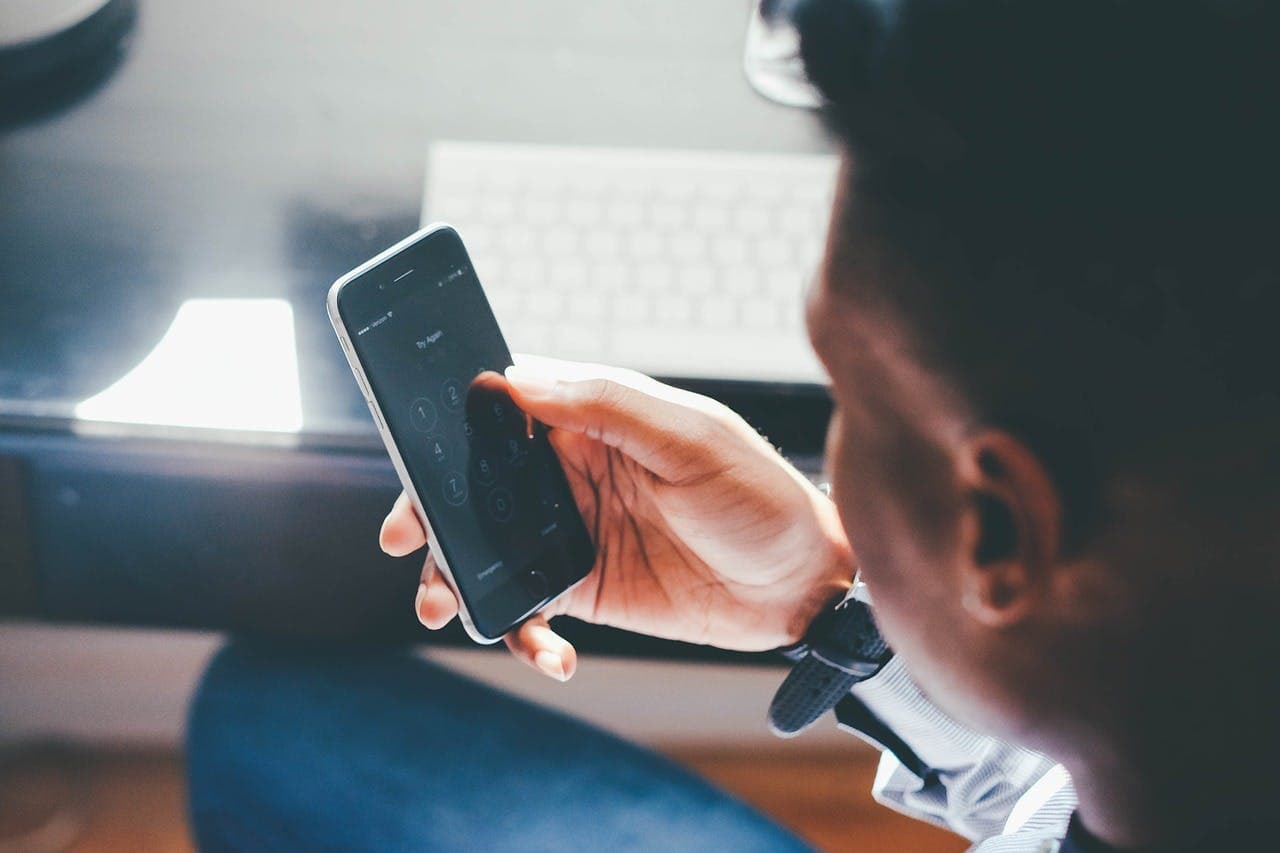 A person types on a smartphone locked screen displaying "Try Again", with a blurred keyboard and desk in the background.