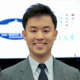Hyunsoo Chang: An Asian Man in a gray suit and blue tie with the logo of the white house in his background.