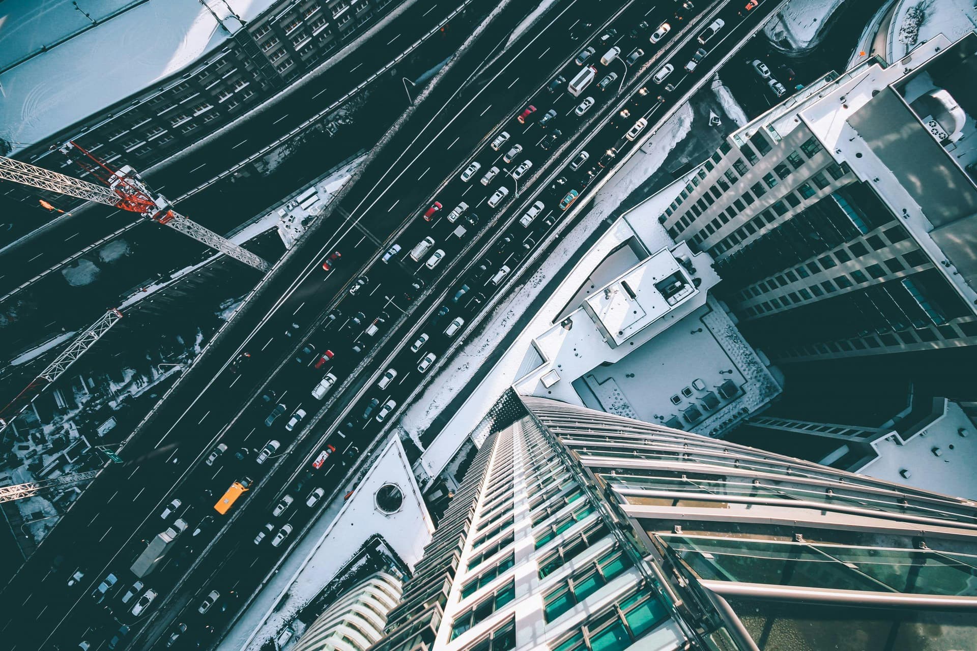 Cars are stuck in traffic on multiple snow-covered highways, seen from an overhead perspective amidst tall buildings and construction cranes.