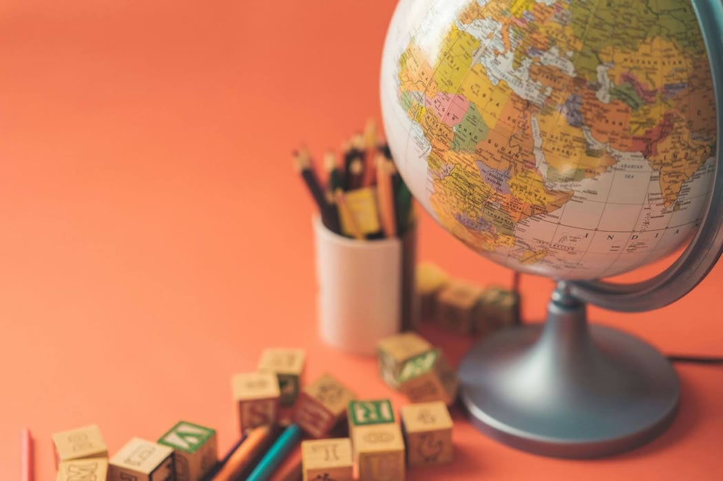 Picture of a globe, colored pencils, and wooden letter blocks against an orange background. 