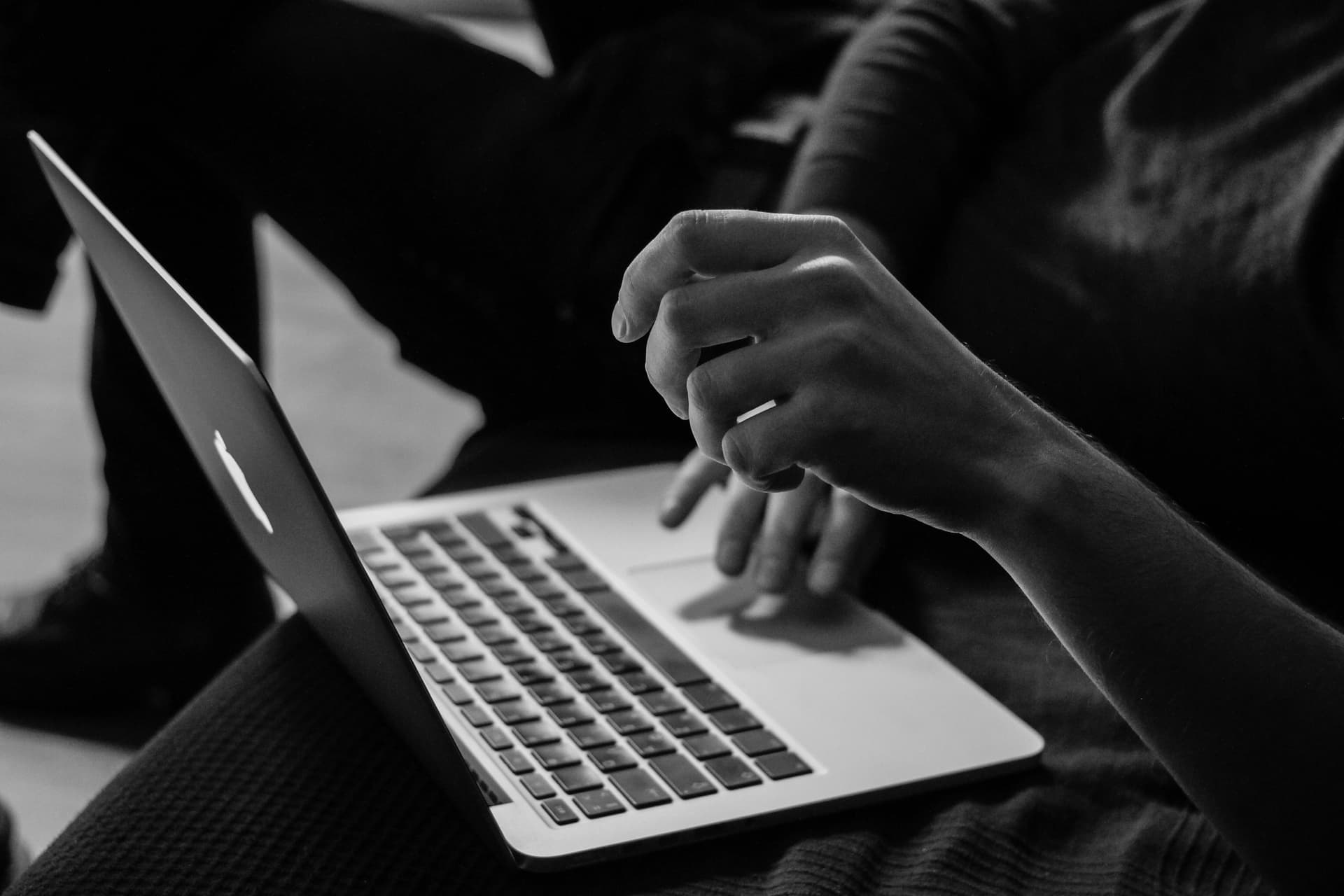 A black-and-white image of a person working on a laptop.