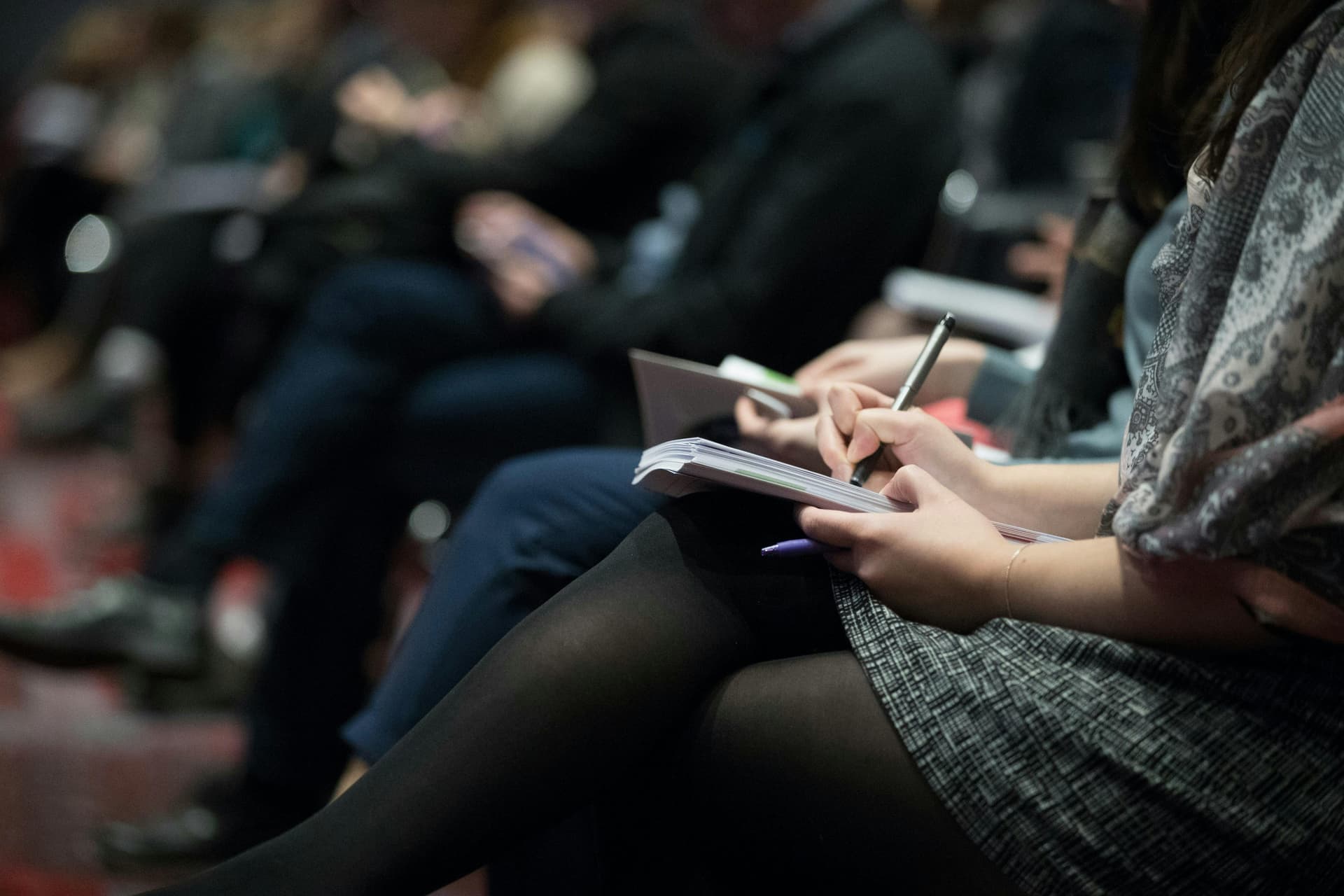 Lower body of a woman sitting in a conference taking notes.
